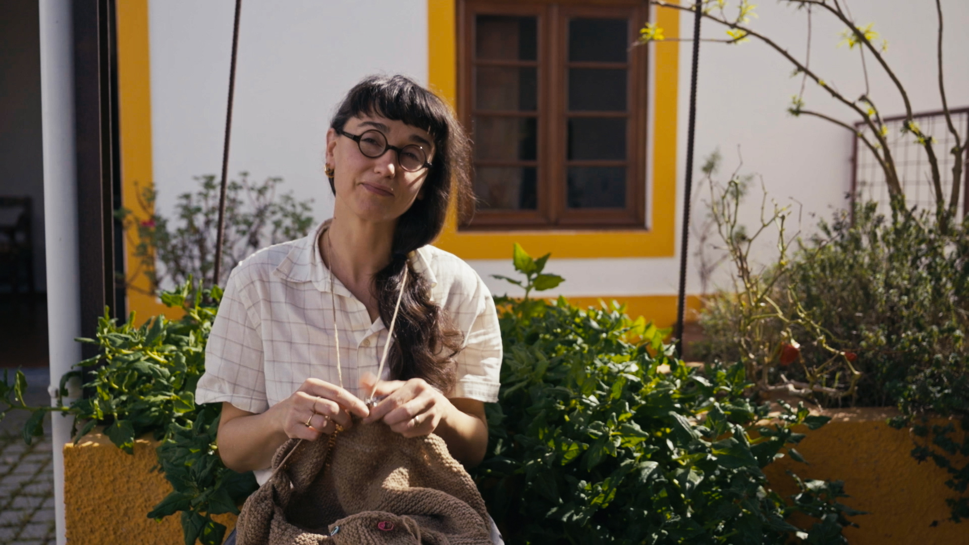 Eine Frau strickt im Freien mit naturfarbenem Wollgarn.